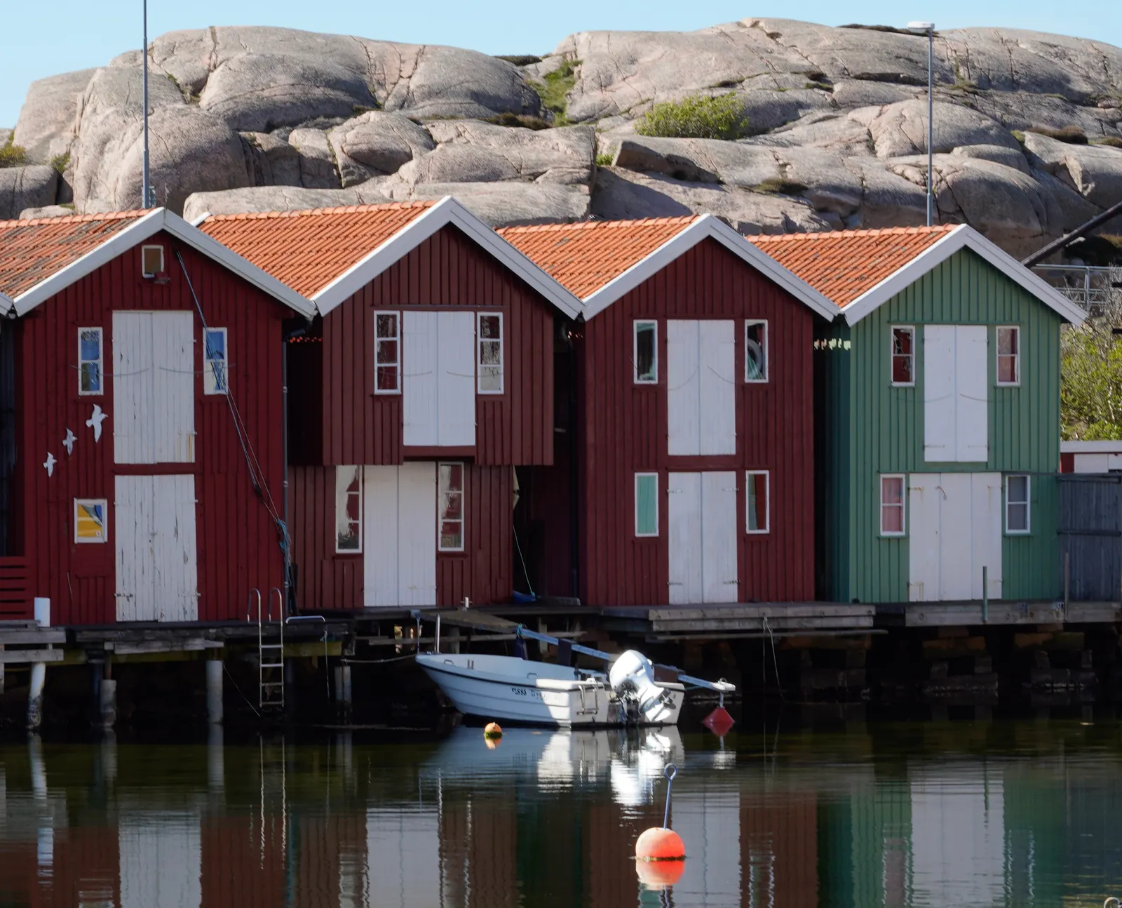 Röda sjöbodar vid vattnet framför granitklippor, typiskt för Bohusläns kust.